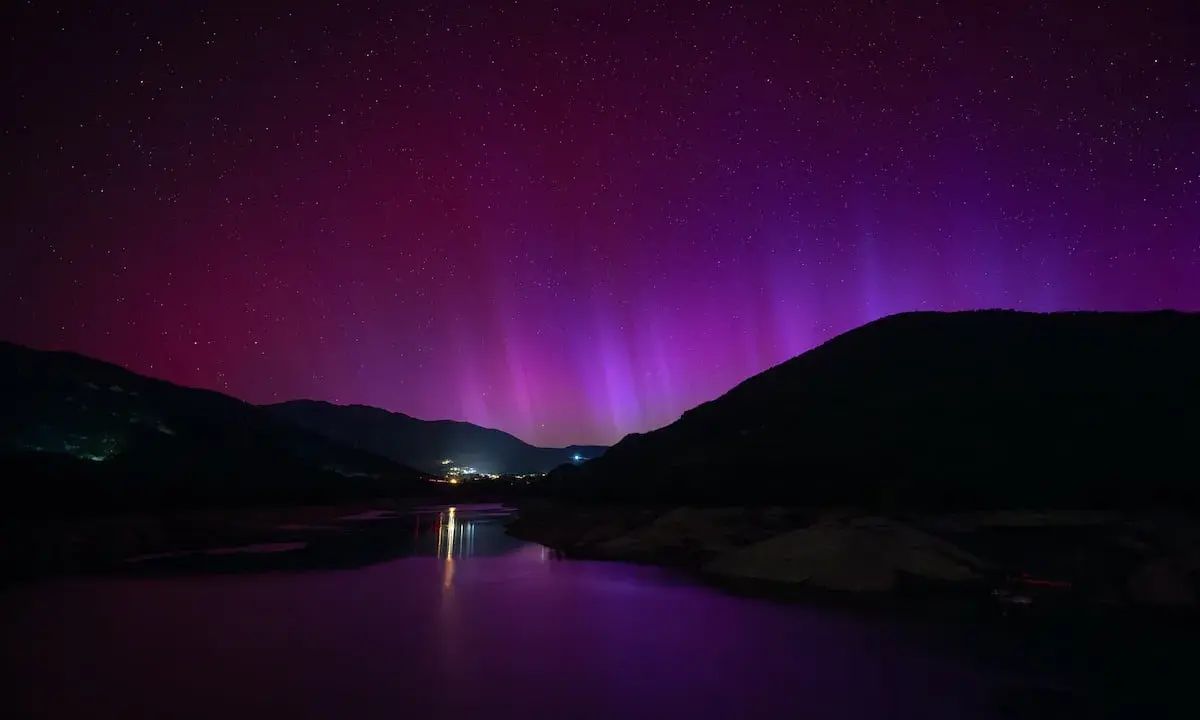 Espectacular aurora boreal en España, tiñendo el cielo de púrpura sobre montañas y un lago.
