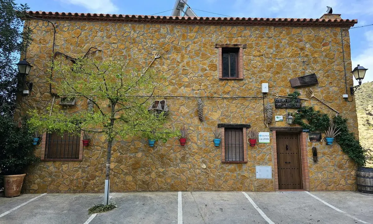 Casa rural "El Balcón del Camino Viejo", fachada de piedra con herramientas de campo y macetas de colores.