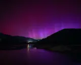 Espectacular aurora boreal en España, tiñendo el cielo de púrpura sobre montañas y un lago.