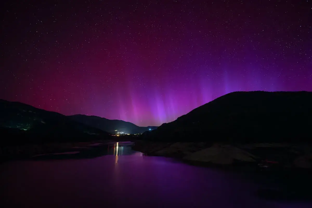 Espectacular aurora boreal en España, tiñendo el cielo de púrpura sobre montañas y un lago.