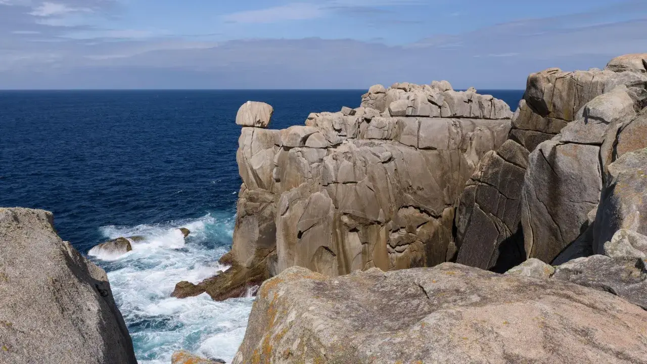 Impresionantes acantilados de papel se alzan sobre el mar azul, con olas rompiendo en su base.