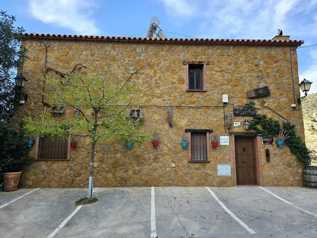 Casa rural "El Balcón del Camino Viejo", fachada de piedra con herramientas de campo y macetas de colores.