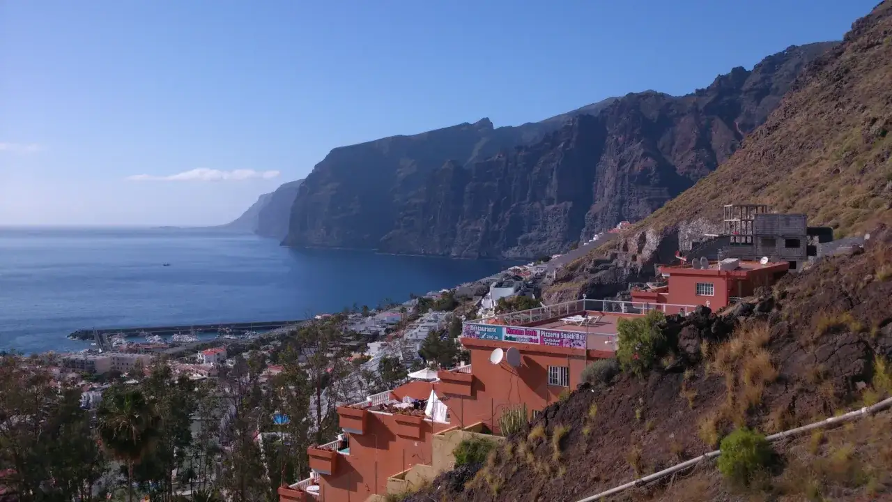 Majestuosos acantilados en España se alzan sobre un mar azul, con un pueblo costero y edificios anaranjados en la ladera.