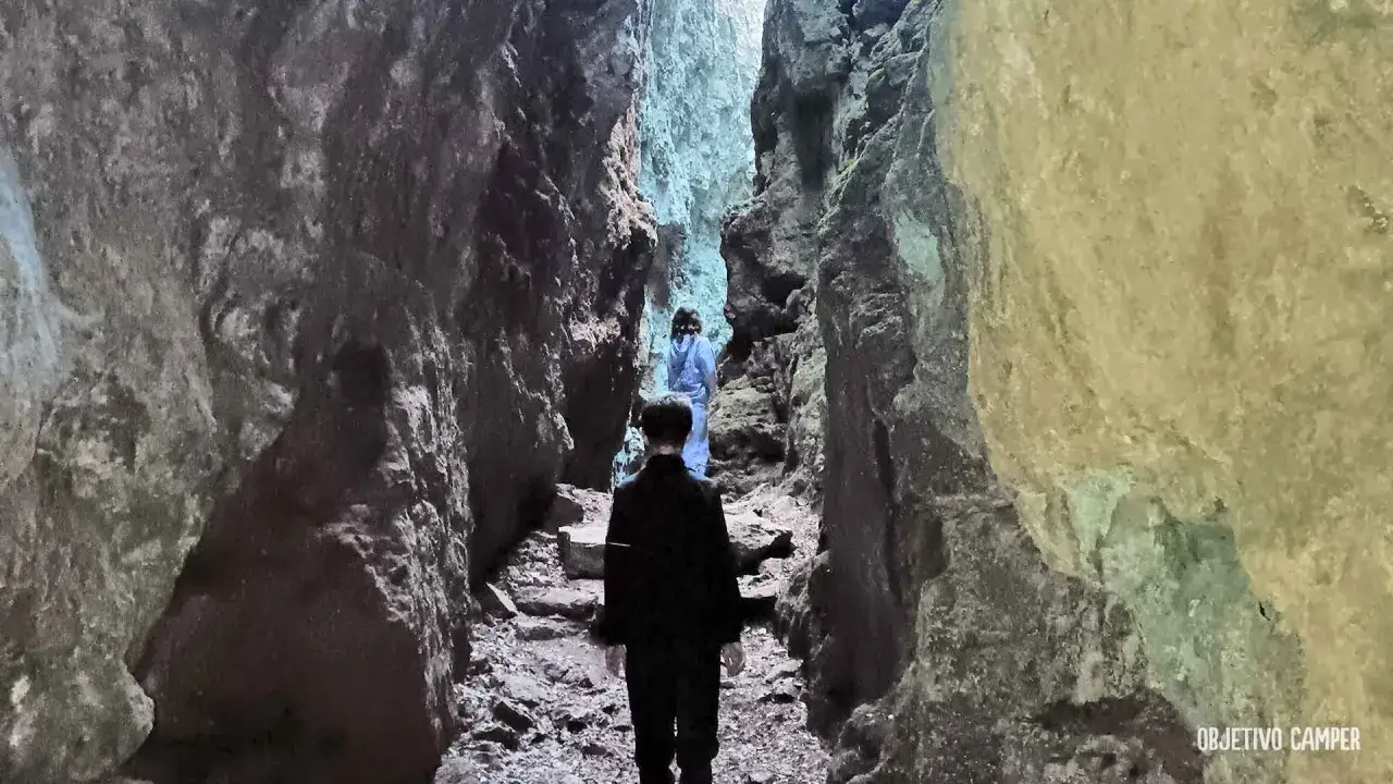 Dos personas caminan por un estrecho sendero entre imponentes rocas, explorando los avencs de la Febró.