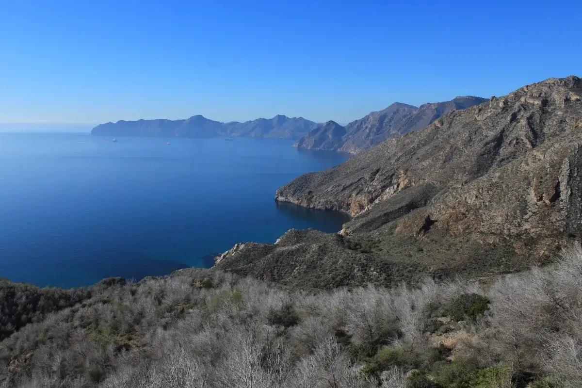 Vista del cabo tiñoso con mar azul intenso y montañas áridas. Barcos navegan en la distancia.