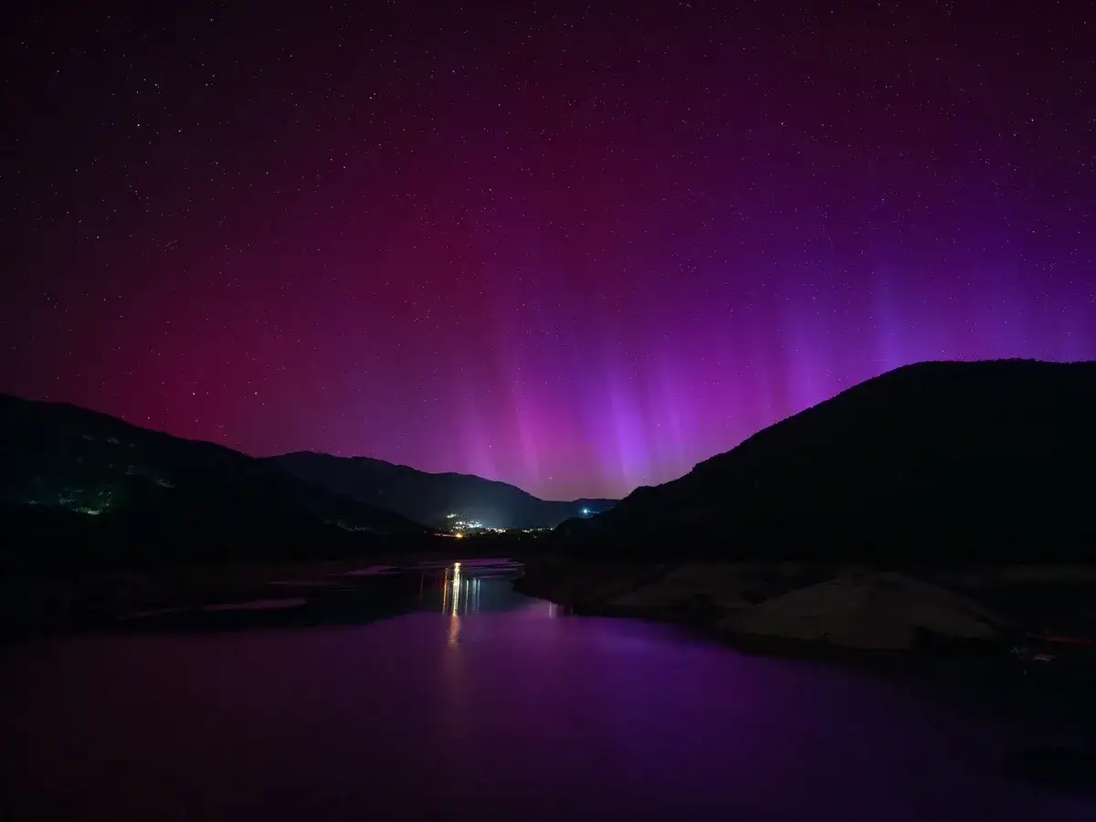 Espectacular aurora boreal en España, tiñendo el cielo de púrpura sobre un paisaje montañoso y un lago.