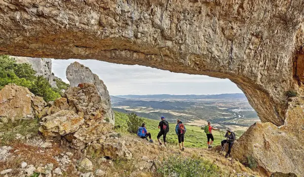 Senderismo Navarra: grupo de excursionistas admira un paisaje montañoso desde debajo de un arco de roca natural.