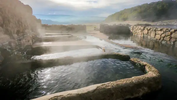 Tierras de vapor y agua en las termas naturales Galicia. Un paisaje sereno con piscinas escalonadas y muros de piedra.