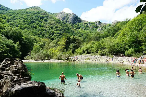 Gente disfrutando del agua cristalina en la olla de San Vicente, rodeada de exuberante vegetación y montañas.
