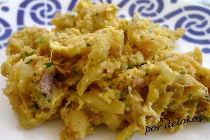 Un plato de alheira que es una deliciosa mezcla desmenuzada de carne, patatas y hierbas, servido en un plato blanco con un patrón azul.