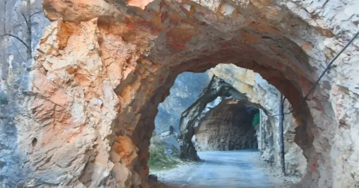 Un túnel natural en la ruta del silencio Teruel, con paredes de roca rojiza y un camino que se adentra en la montaña.