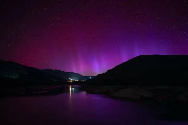 Espectacular aurora boreal en España, tiñendo el cielo de púrpura sobre montañas y un lago.