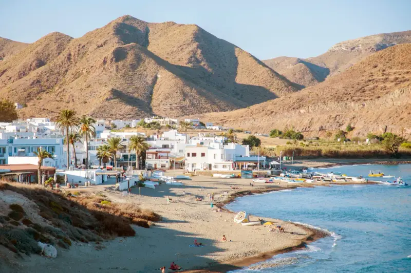 Pueblos de Almería con playa, casas blancas y palmeras junto a un mar azul, con montañas áridas de fondo.